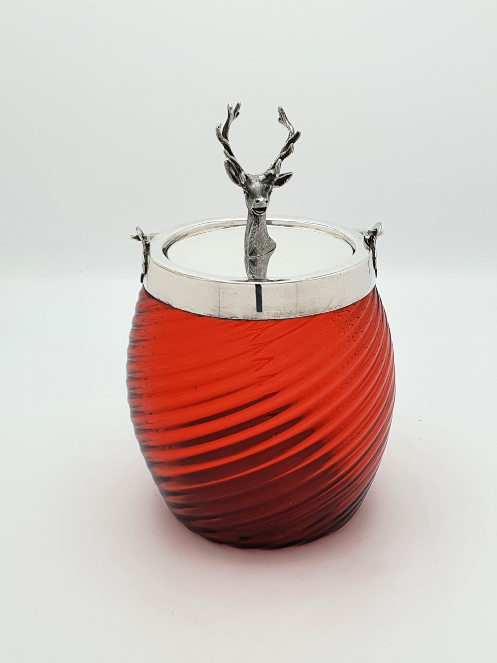 A Victorian ribbed cranberry red glass biscuit barrel featuring a silver-plated rim, handle mounts, and a lid surmounted by a stag head finial.