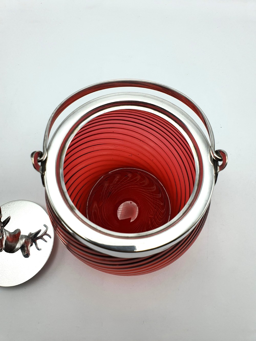 A Victorian ribbed cranberry red glass biscuit barrel featuring a silver-plated rim, handle mounts, and a lid surmounted by a stag head finial. View III