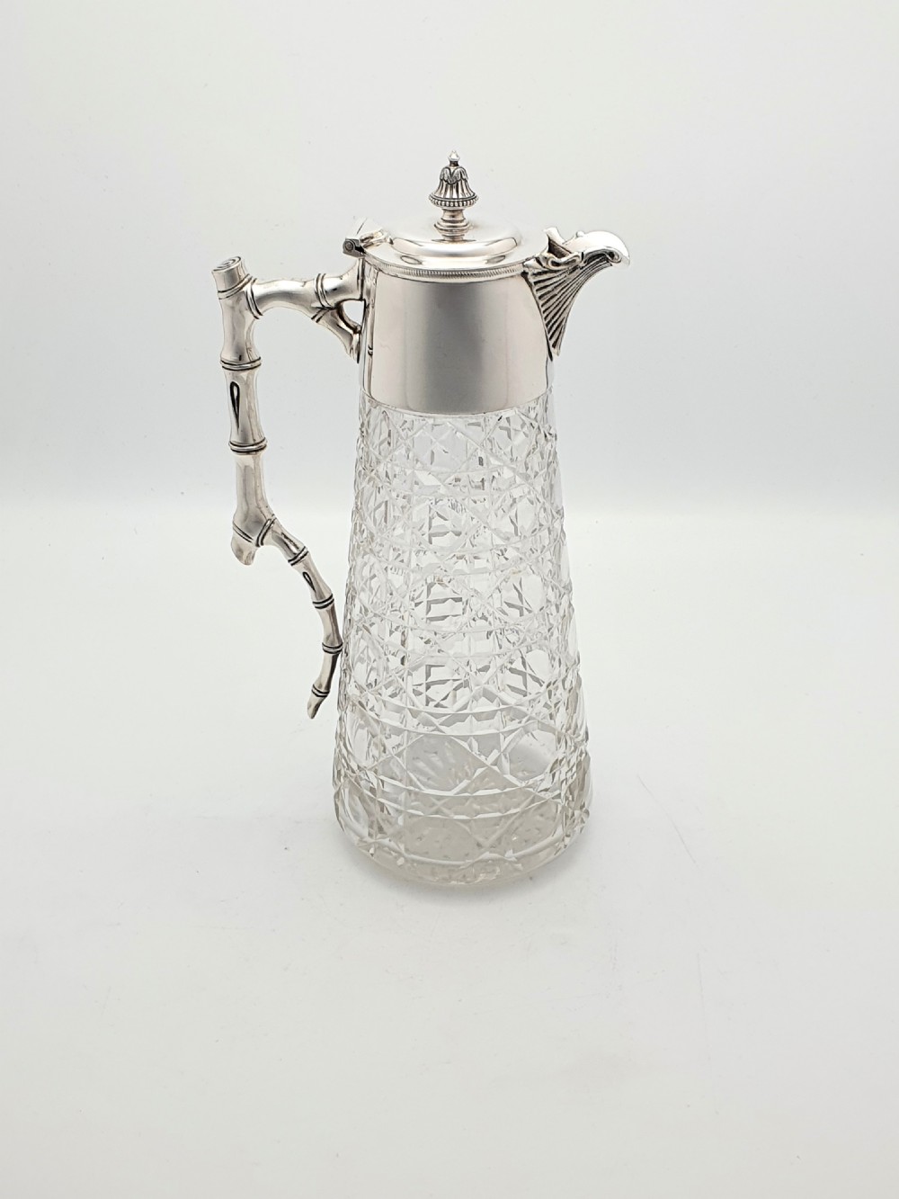 An Edwardian tapered cut glass claret jug with a diamond pattern, silver-plated collar, hinged lid, and a faux-bamboo handle.