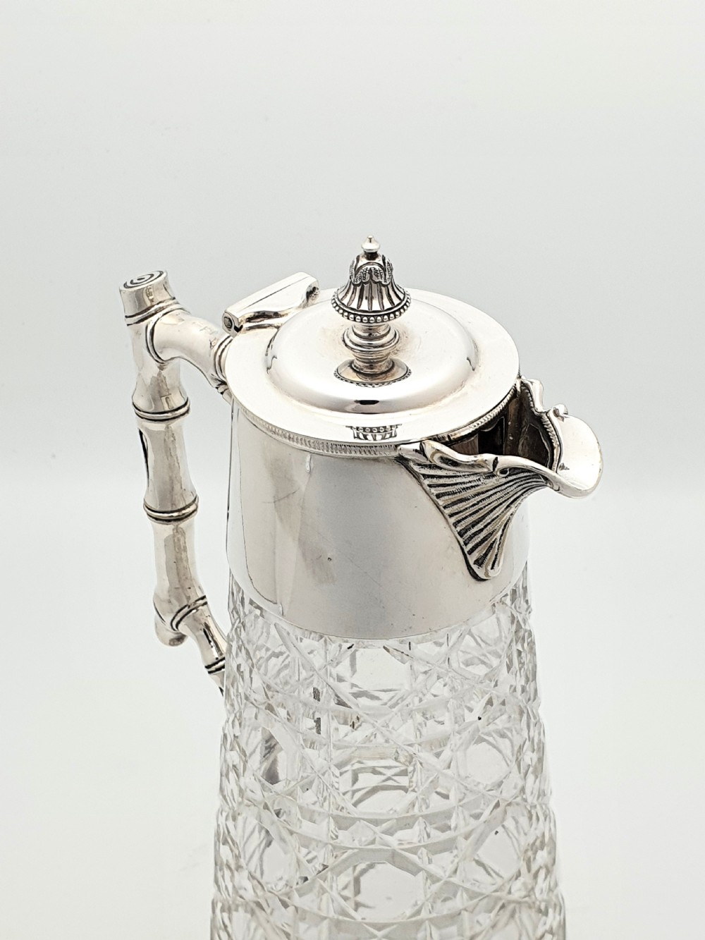 An Edwardian tapered cut glass claret jug with a diamond pattern, silver-plated collar, hinged lid, and a faux-bamboo handle. View V