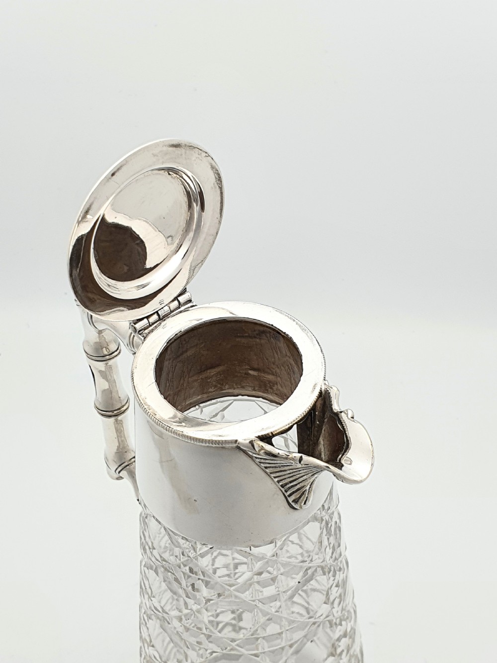 An Edwardian tapered cut glass claret jug with a diamond pattern, silver-plated collar, hinged lid, and a faux-bamboo handle. View VI