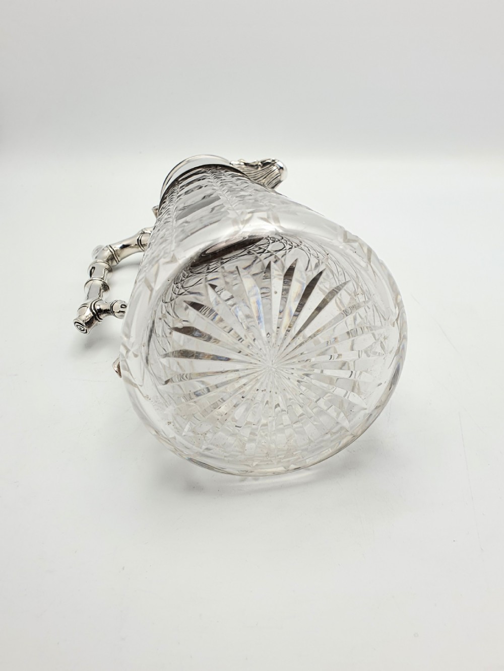 An Edwardian tapered cut glass claret jug with a diamond pattern, silver-plated collar, hinged lid, and a faux-bamboo handle. View VII