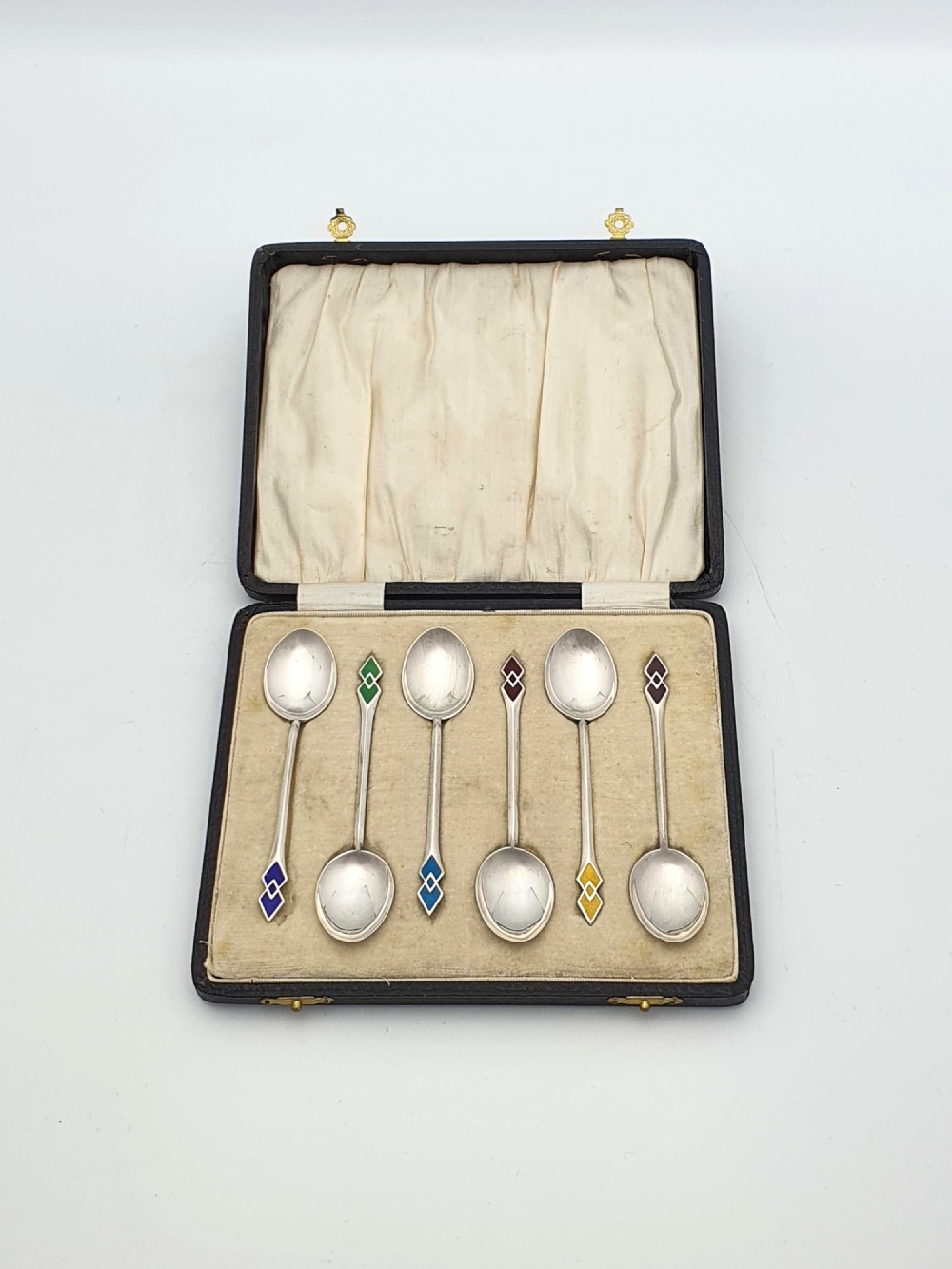 A set of six silver Art Deco teaspoons featuring geometric enamel terminals in a black velvet and satin fitted presentation case.