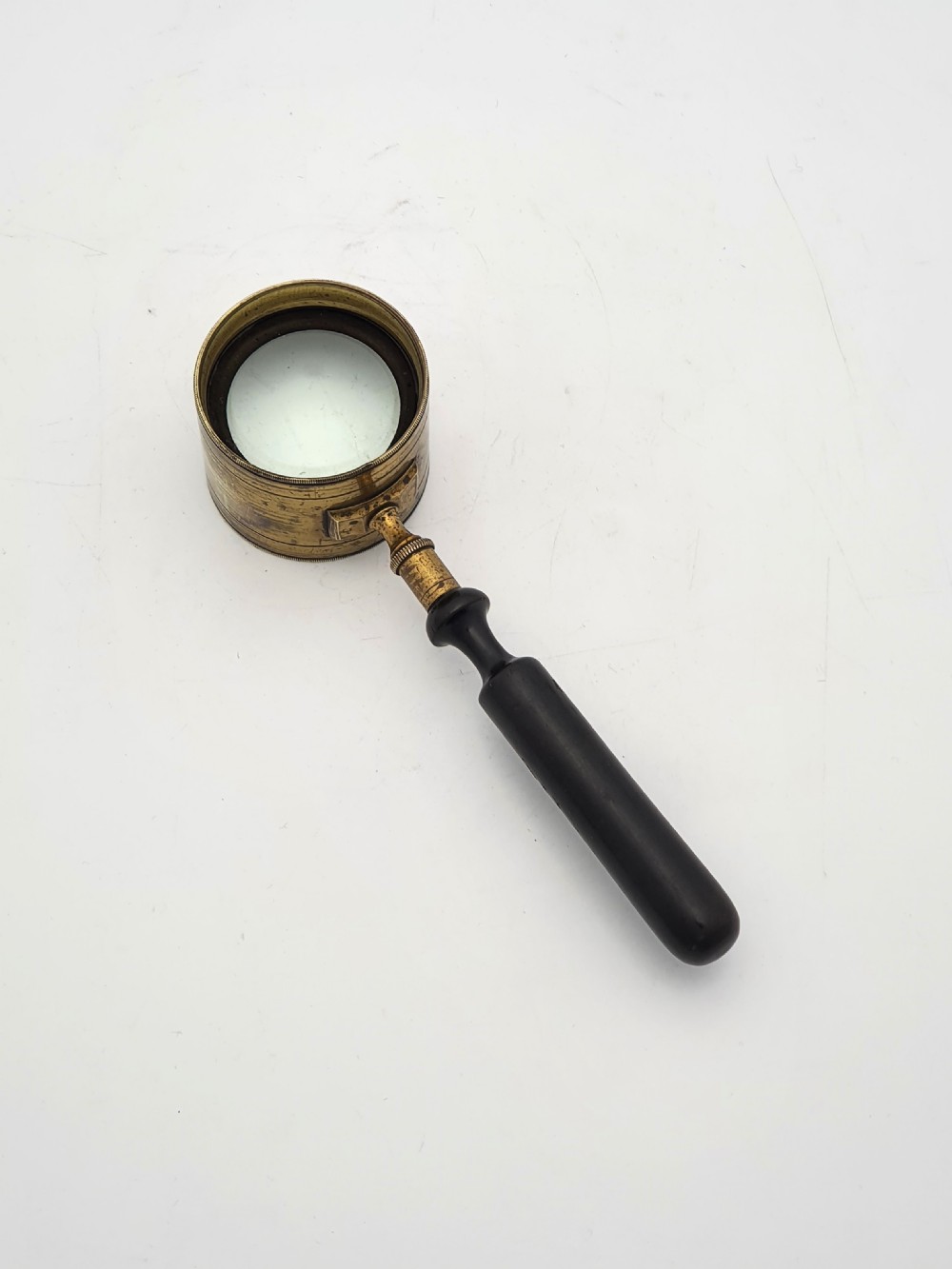 Victorian Coddington scientific magnifying glass with a thick cylindrical brass lens collar and turned black ebonised wooden handle on a white background.