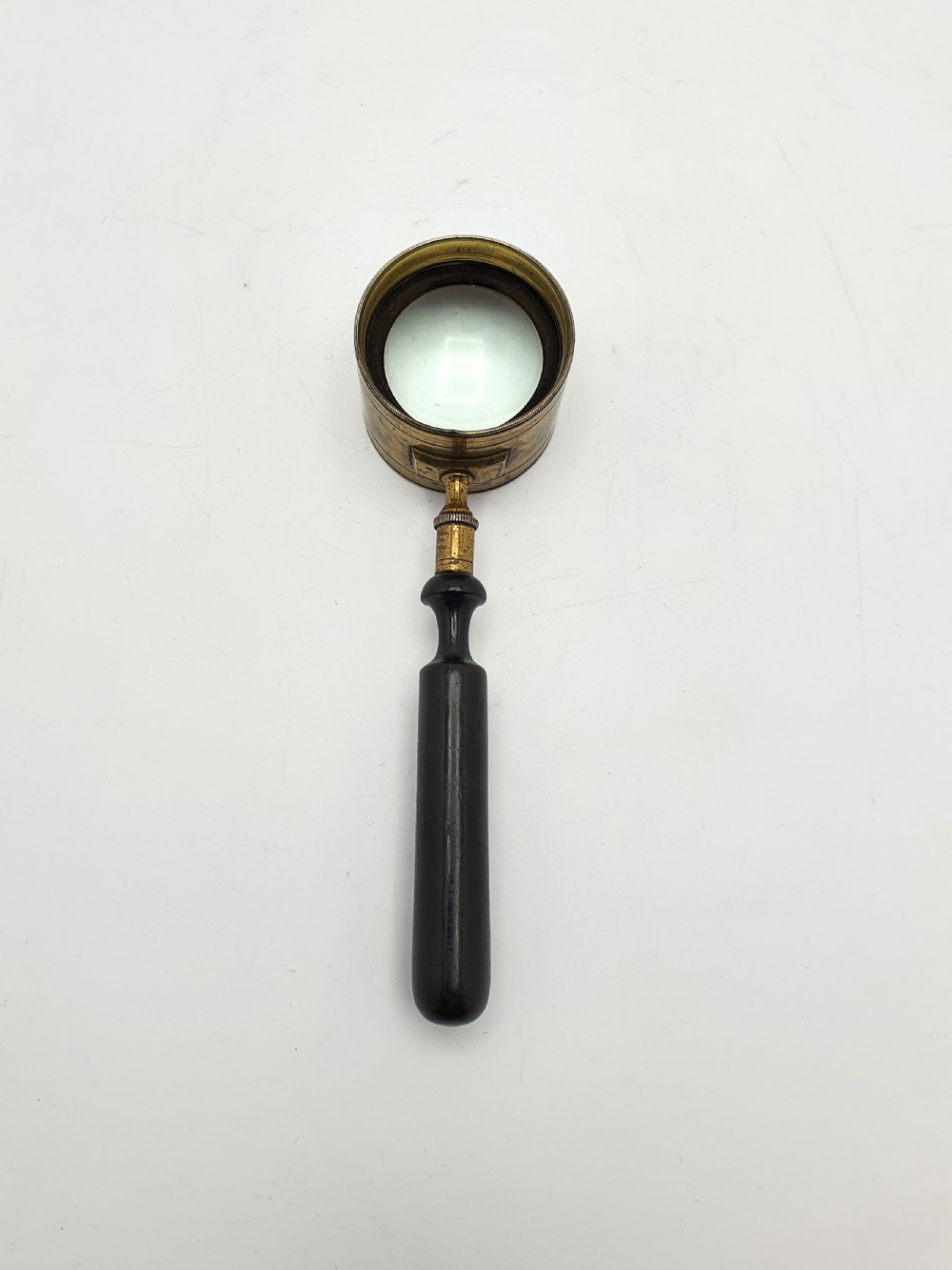 Victorian Coddington scientific magnifying glass with a thick cylindrical brass lens collar and turned black ebonised wooden handle on a white background. View II