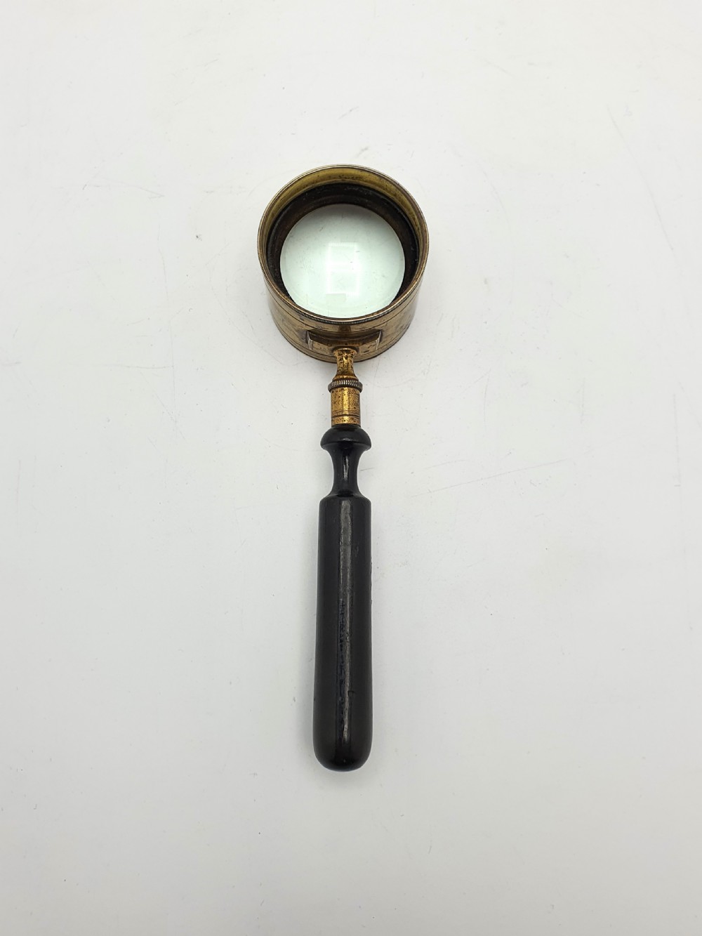 Victorian Coddington scientific magnifying glass with a thick cylindrical brass lens collar and turned black ebonised wooden handle on a white background. View III