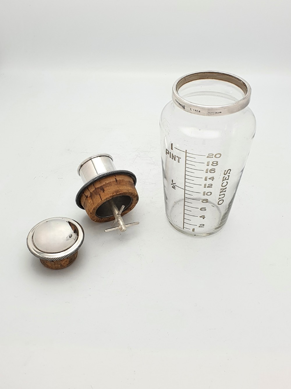 A clear glass cocktail shaker with etched fluid ounce measurement markings, fitted with a cork seal and a polished silver-plated cap. View III