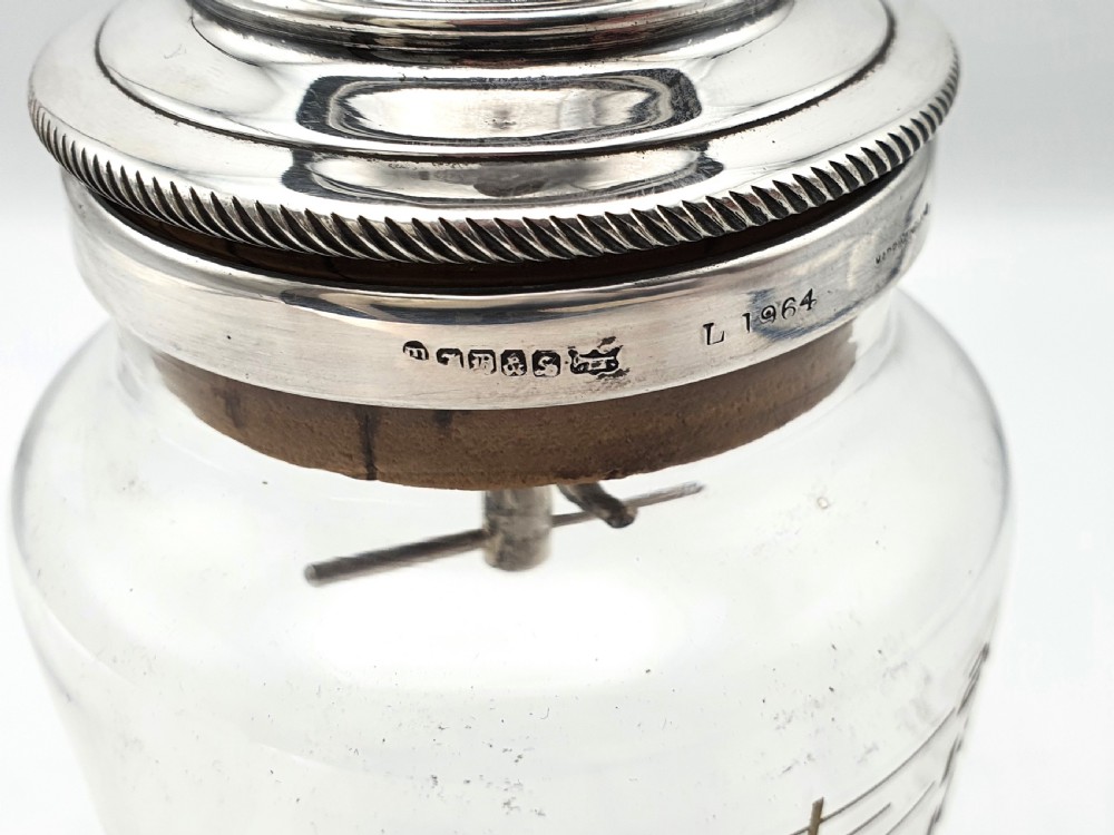 A clear glass cocktail shaker with etched fluid ounce measurement markings, fitted with a cork seal and a polished silver-plated cap. View VI