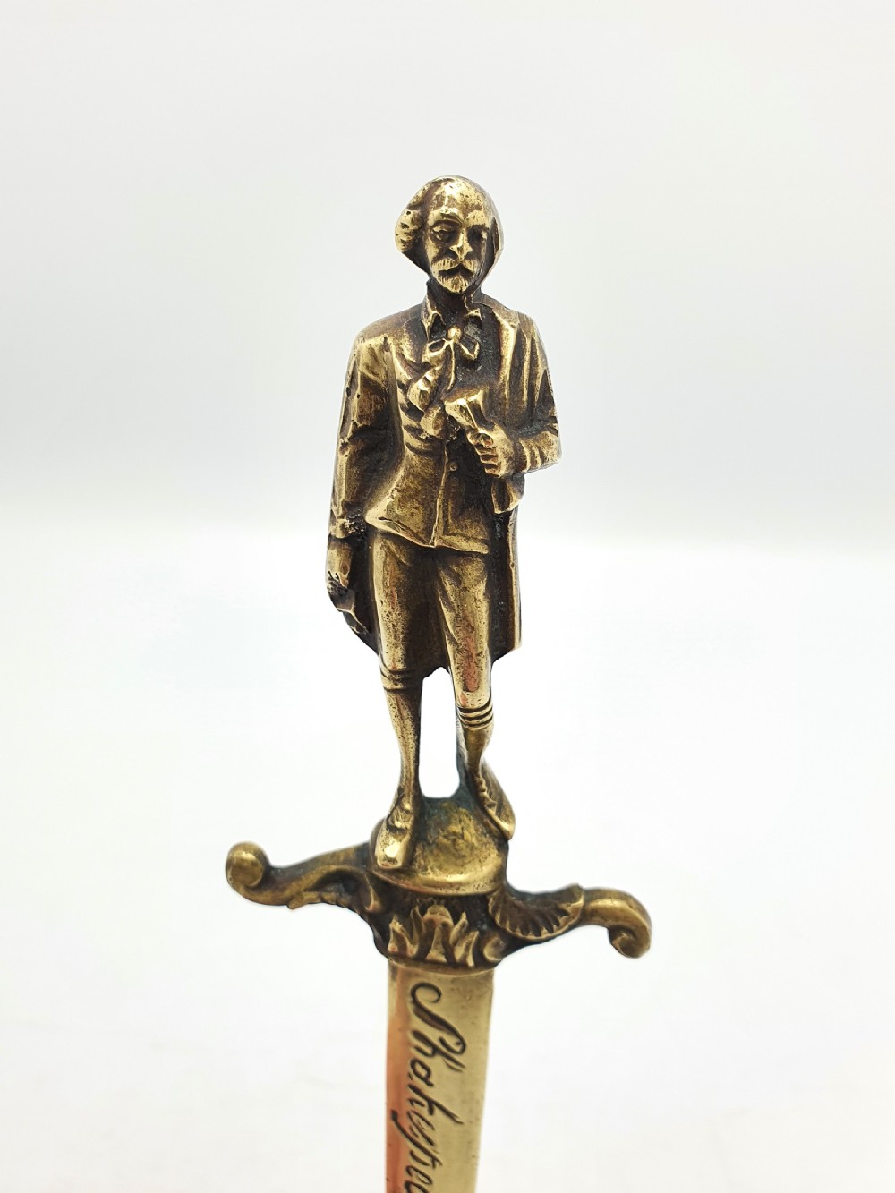 An antique brass letter opener shaped like a dagger featuring a sculpted figure of William Shakespeare on the handle and his name engraved on the blade. View II