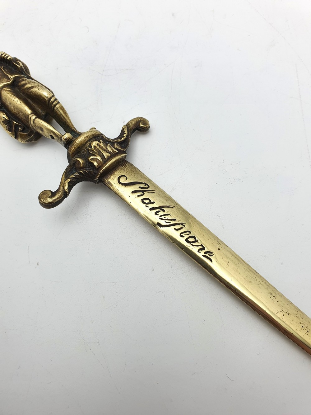 An antique brass letter opener shaped like a dagger featuring a sculpted figure of William Shakespeare on the handle and his name engraved on the blade. View V