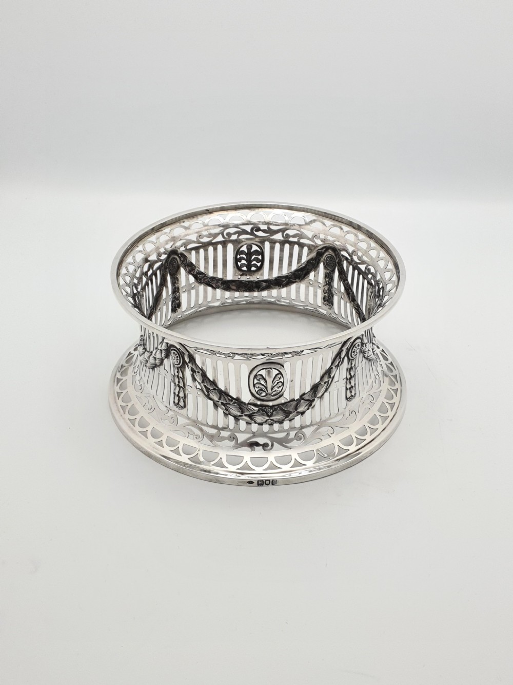 An Edwardian pierced sterling silver dish ring featuring draped swags, vertical slats, oval medallions, and decorative scroll rims on a waisted spool body.
