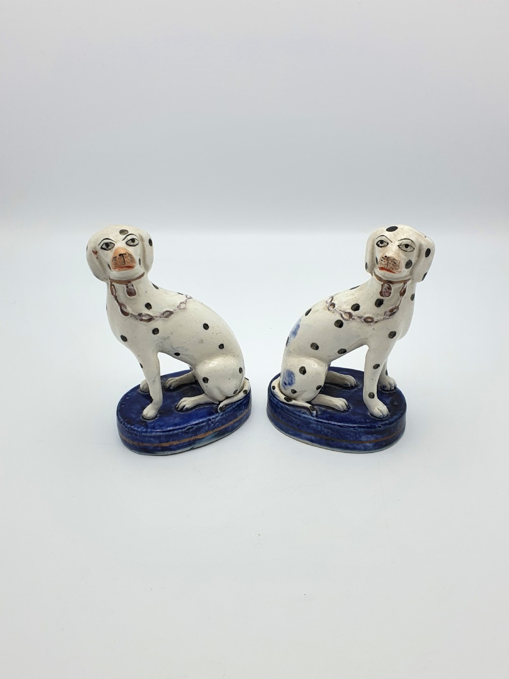 A pair of late Victorian Staffordshire earthenware figures depicting seated Dalmatians with hand-painted black spots on cobalt blue bases.