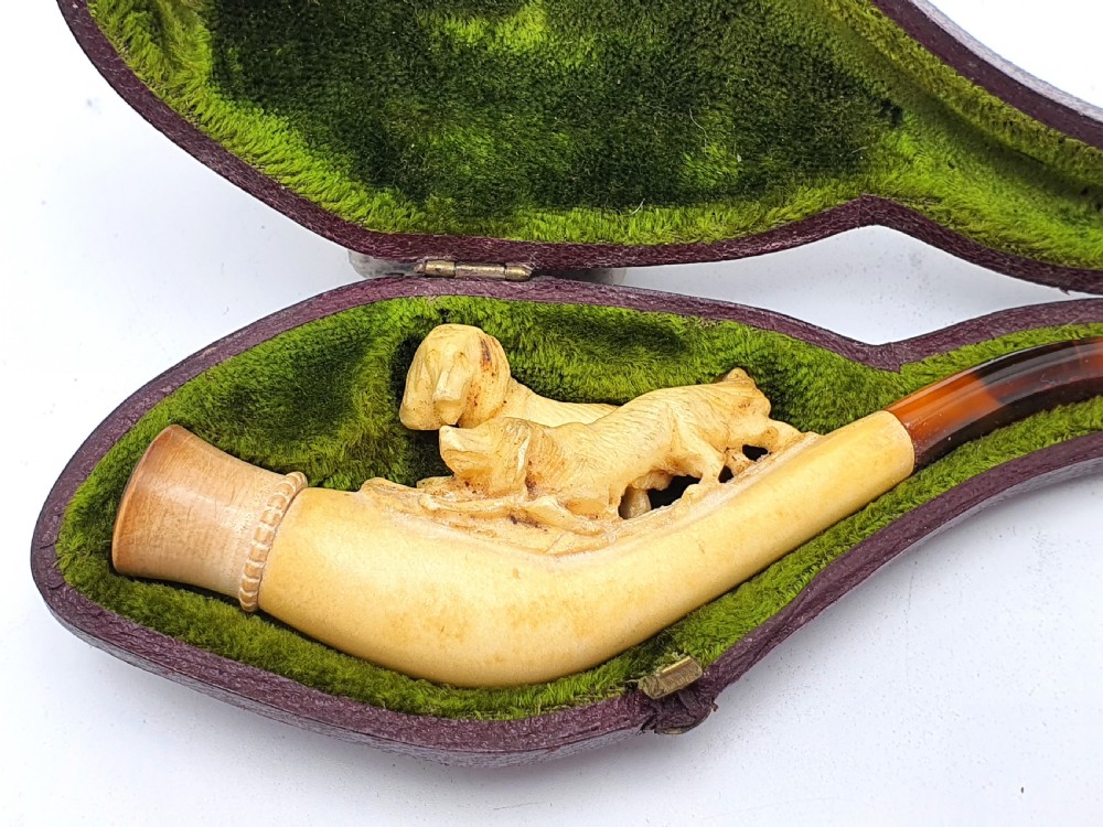 An antique carved meerschaum cheroot holder featuring detailed hunting dogs resting inside a green velvet-lined fitted case. View II