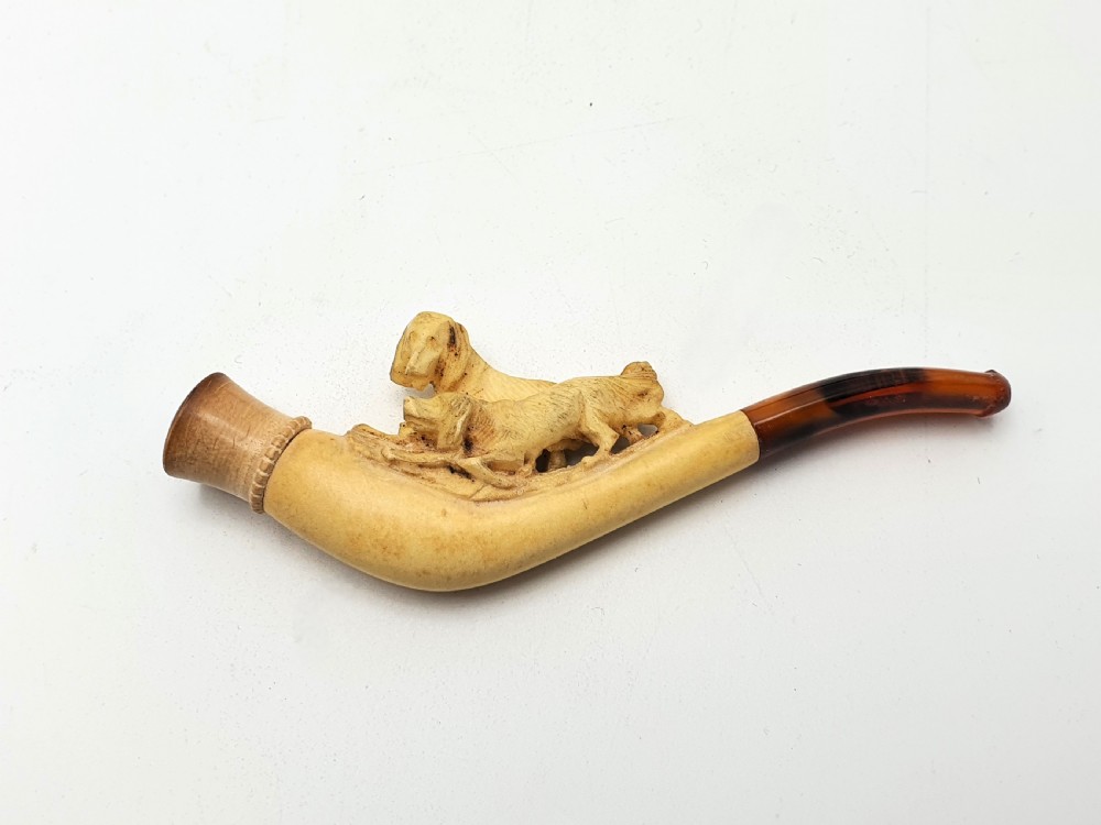An antique carved meerschaum cheroot holder featuring detailed hunting dogs resting inside a green velvet-lined fitted case. View III