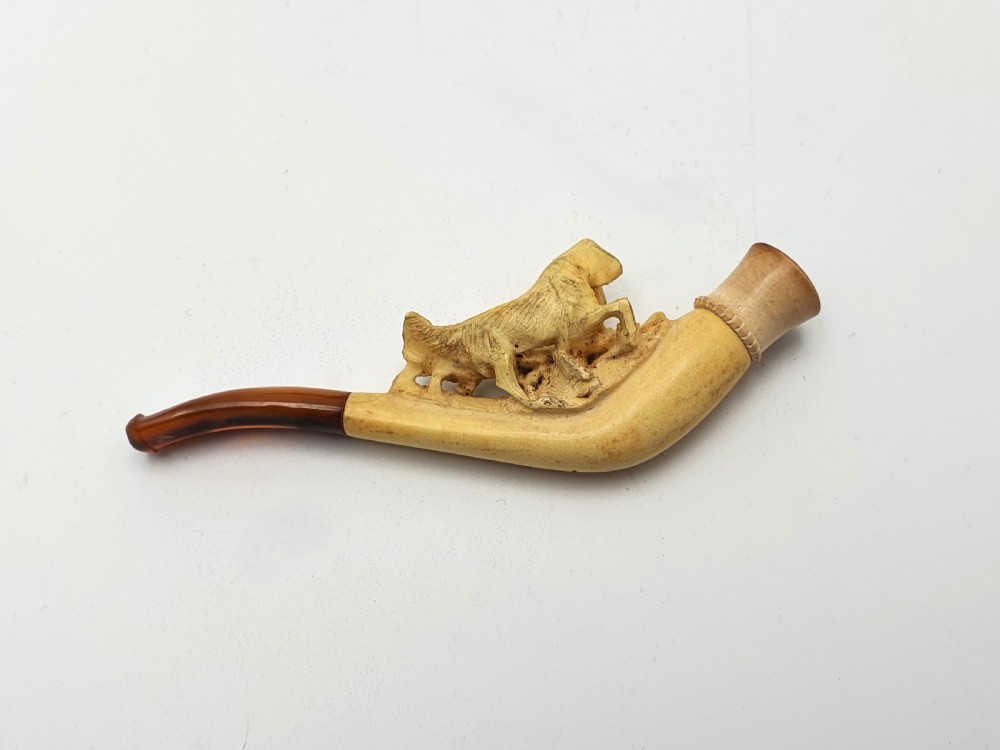 An antique carved meerschaum cheroot holder featuring detailed hunting dogs resting inside a green velvet-lined fitted case. View IV
