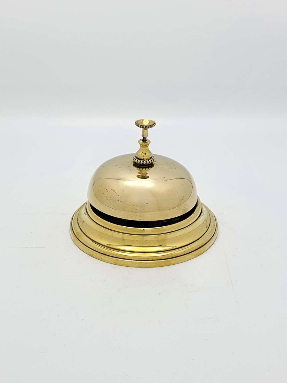 A polished Victorian brass counter bell featuring a circular stepped base, a hemispherical dome shell, and a central knurled push button.