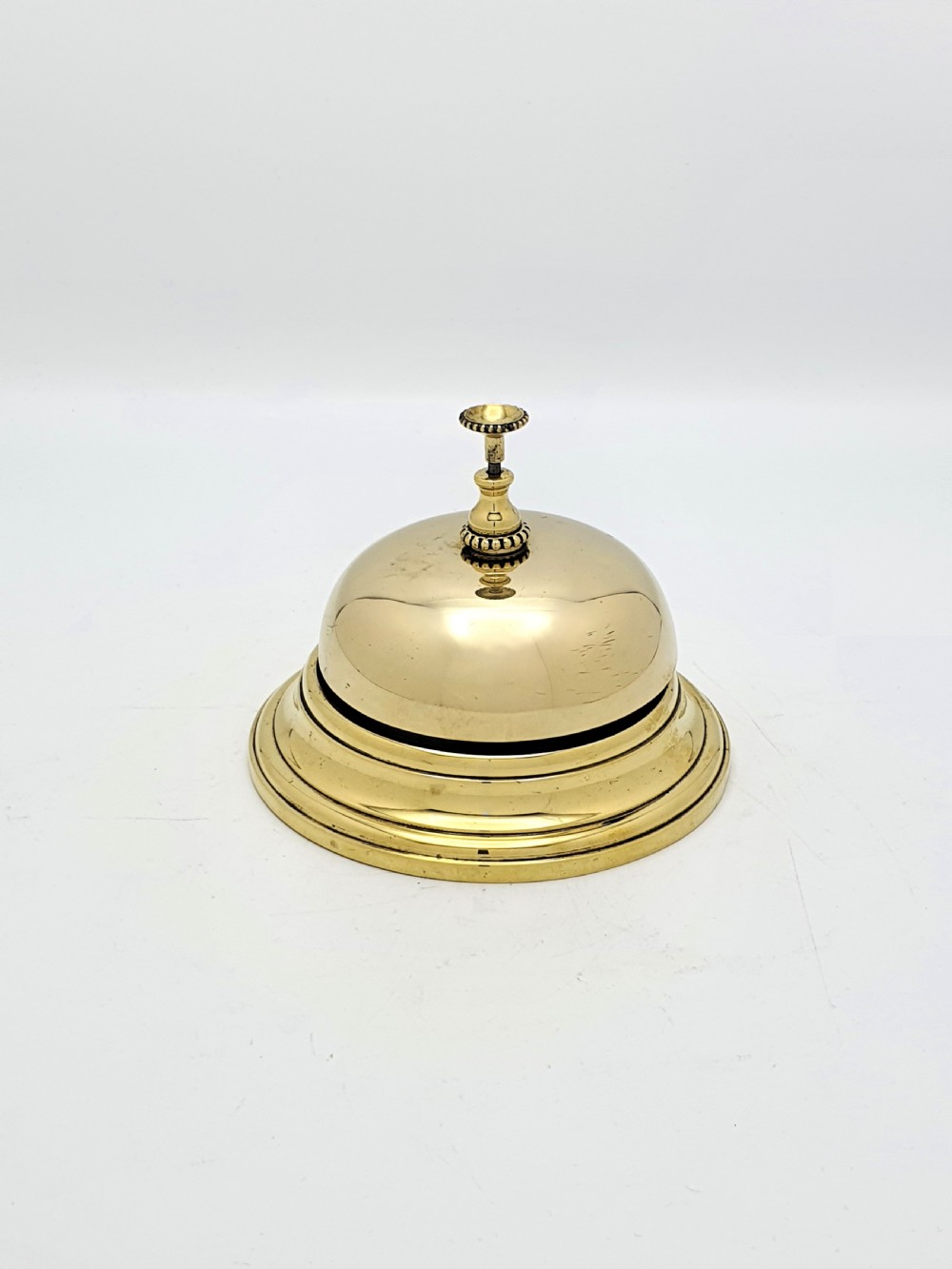 A polished Victorian brass counter bell featuring a circular stepped base, a hemispherical dome shell, and a central knurled push button. View II
