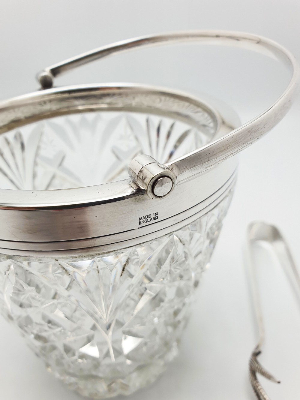 A cut glass ice bucket with a silver-plated rim and carrying handle, resting beside a pair of silver-plated ice tongs with claw tips. View IX