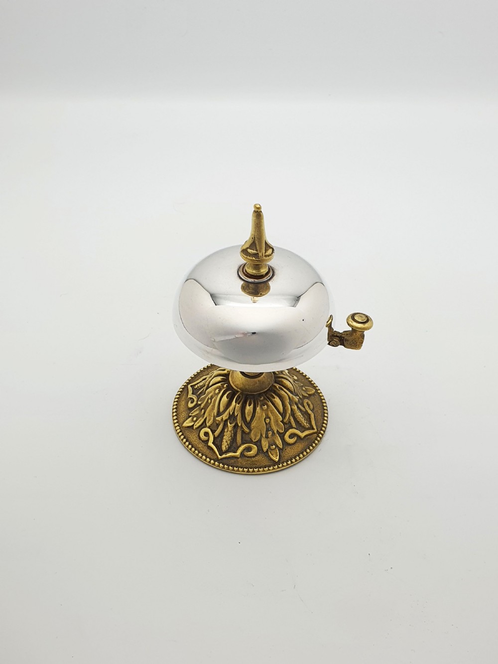 A silver-plated dome desk bell with a brass plunger mechanism mounted on an ornate circular brass base decorated with acanthus leaf motifs. View II