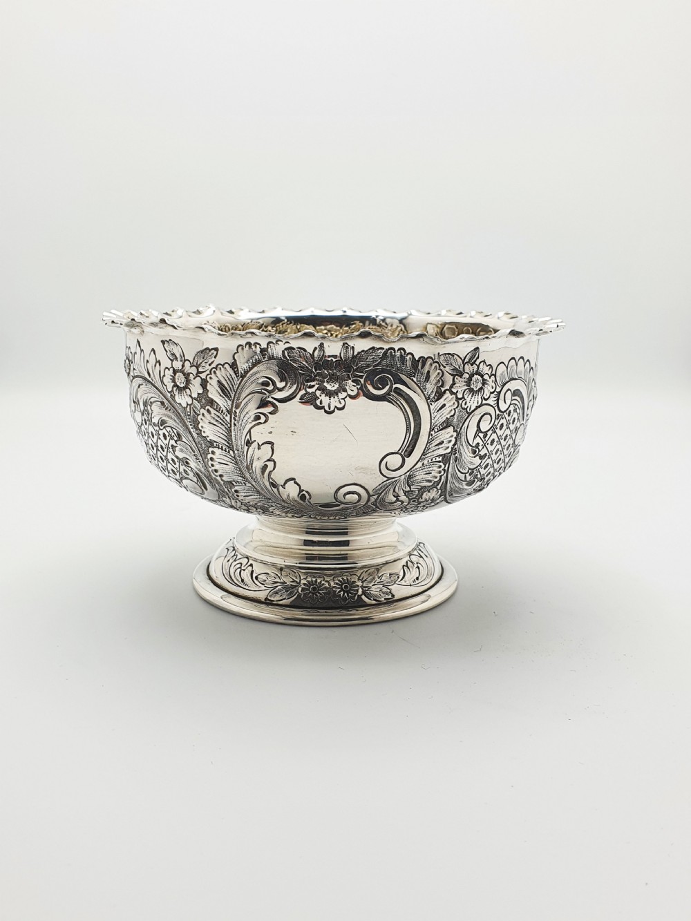 A circular Victorian sterling silver bowl featuring ornate repousse floral chasing, a crimped fluted rim, and a raised pedestal foot. View V