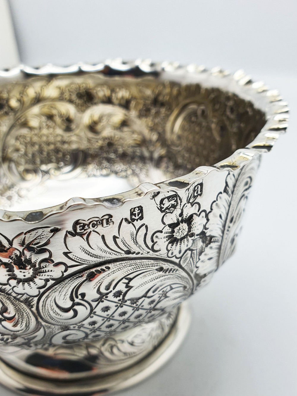 A circular Victorian sterling silver bowl featuring ornate repousse floral chasing, a crimped fluted rim, and a raised pedestal foot. View VI