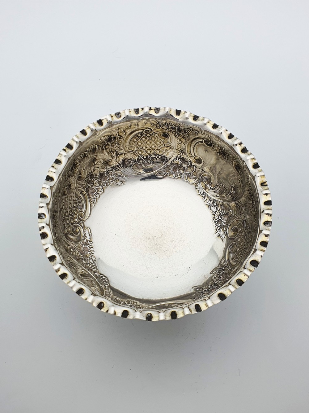 A circular Victorian sterling silver bowl featuring ornate repousse floral chasing, a crimped fluted rim, and a raised pedestal foot. View VII