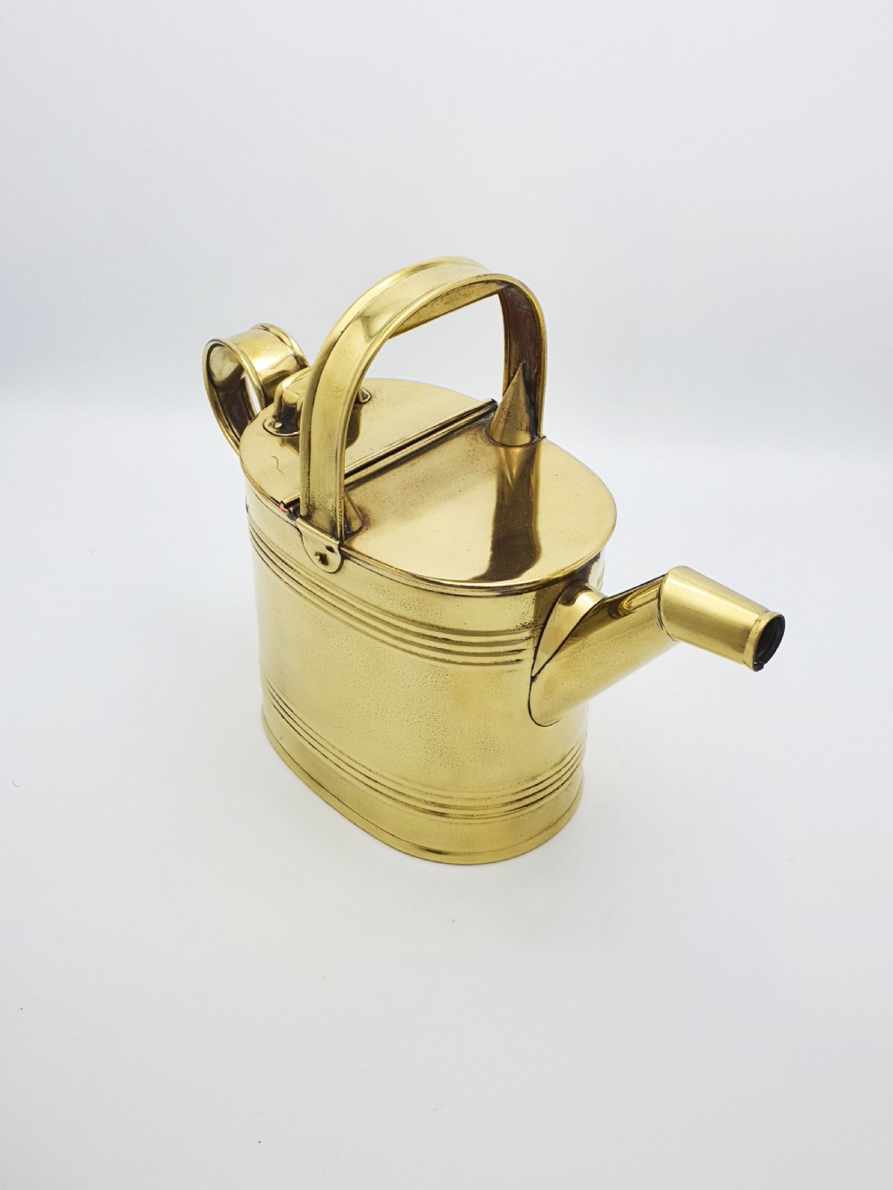 A polished late Victorian brass watering can with an oval body, a curved upper bridge handle, a rear loop handle, and a straight tapered spout.
