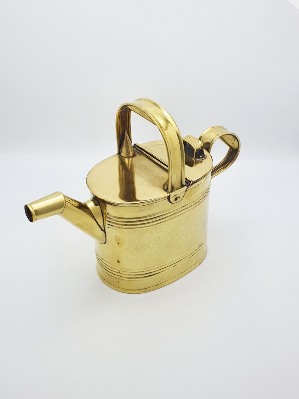 A polished late Victorian brass watering can with an oval body, a curved upper bridge handle, a rear loop handle, and a straight tapered spout. View III