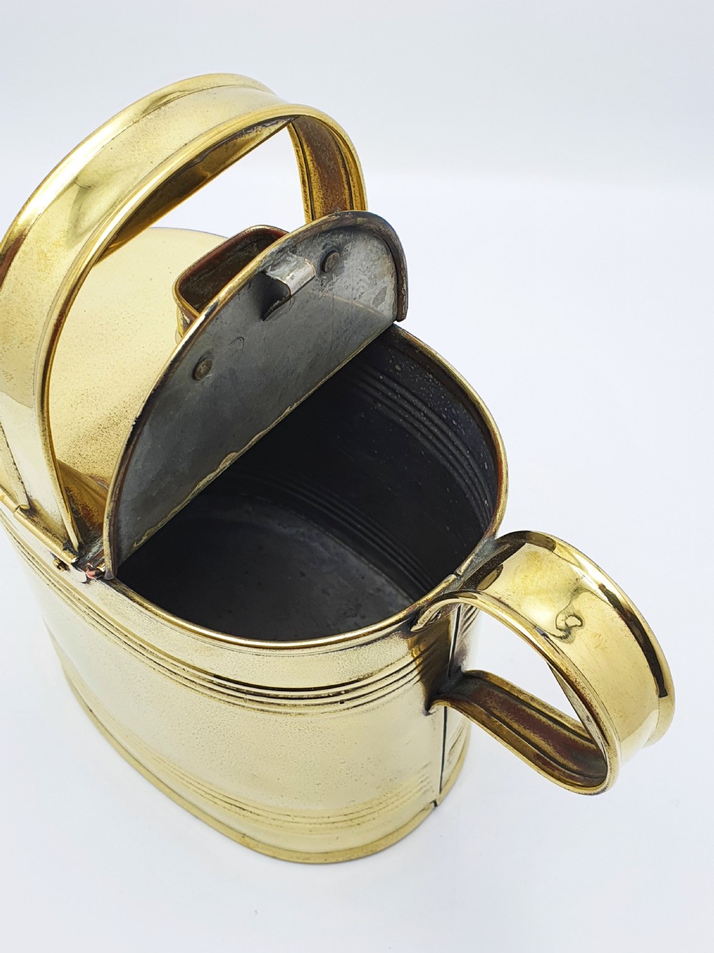 A polished late Victorian brass watering can with an oval body, a curved upper bridge handle, a rear loop handle, and a straight tapered spout. View VII