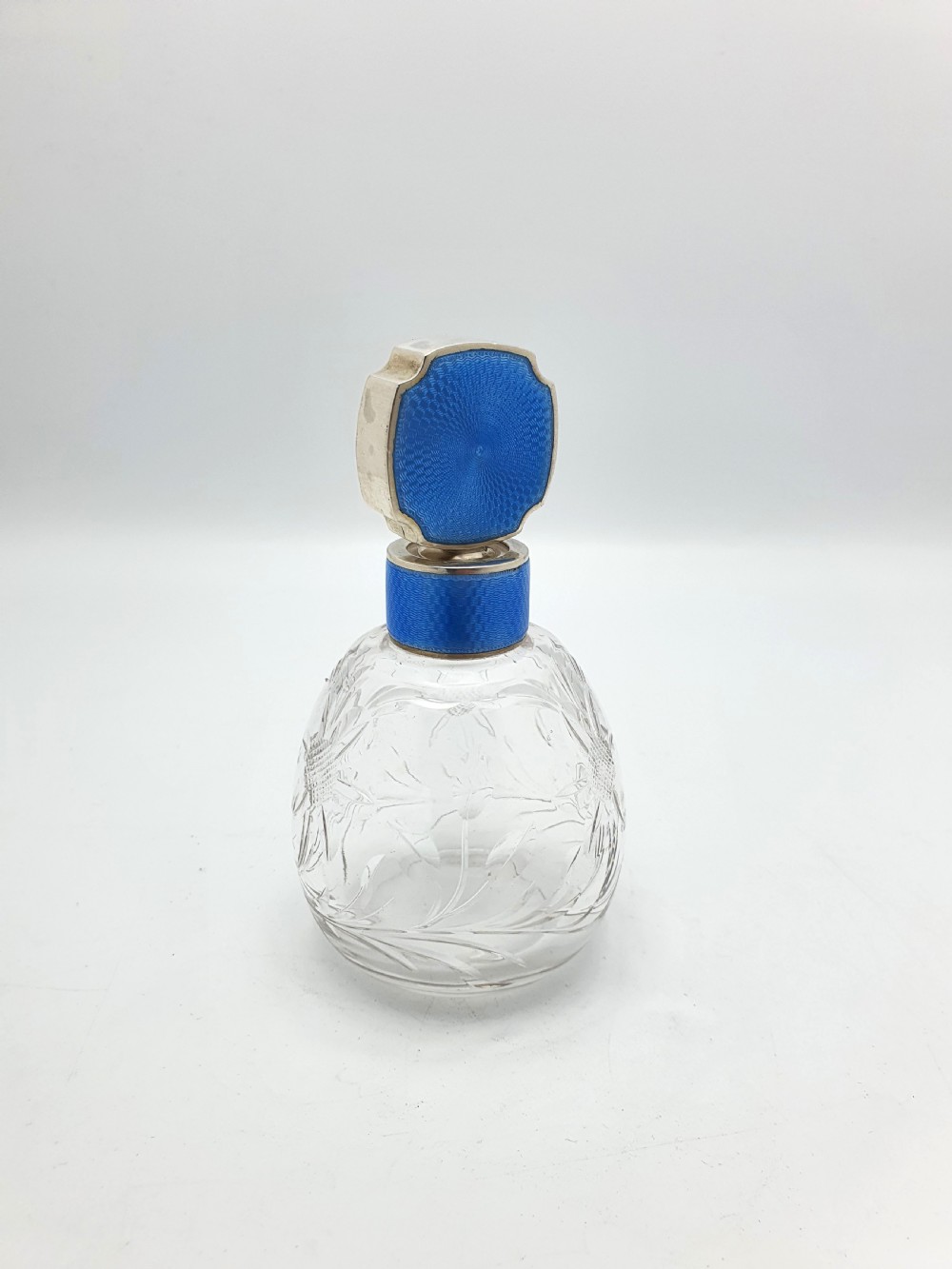 A clear cut glass scent bottle featuring a bright blue guilloche enamel collar and matching octagonal stopper set in sterling silver.
