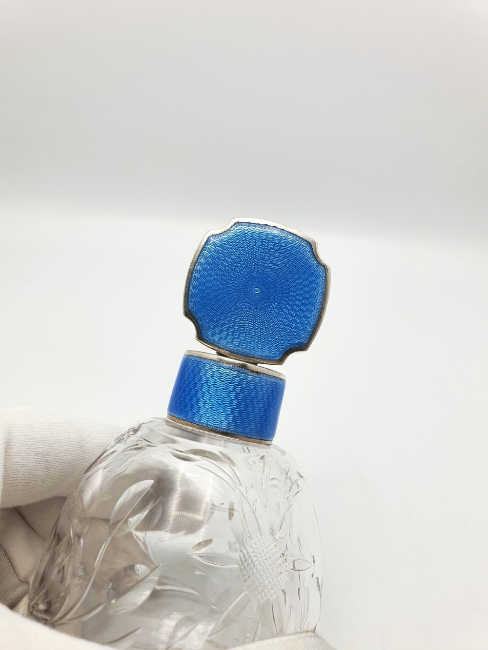 A clear cut glass scent bottle featuring a bright blue guilloche enamel collar and matching octagonal stopper set in sterling silver. View II