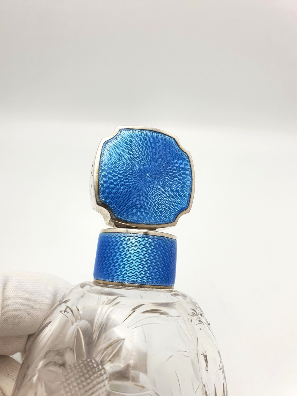 A clear cut glass scent bottle featuring a bright blue guilloche enamel collar and matching octagonal stopper set in sterling silver. View V