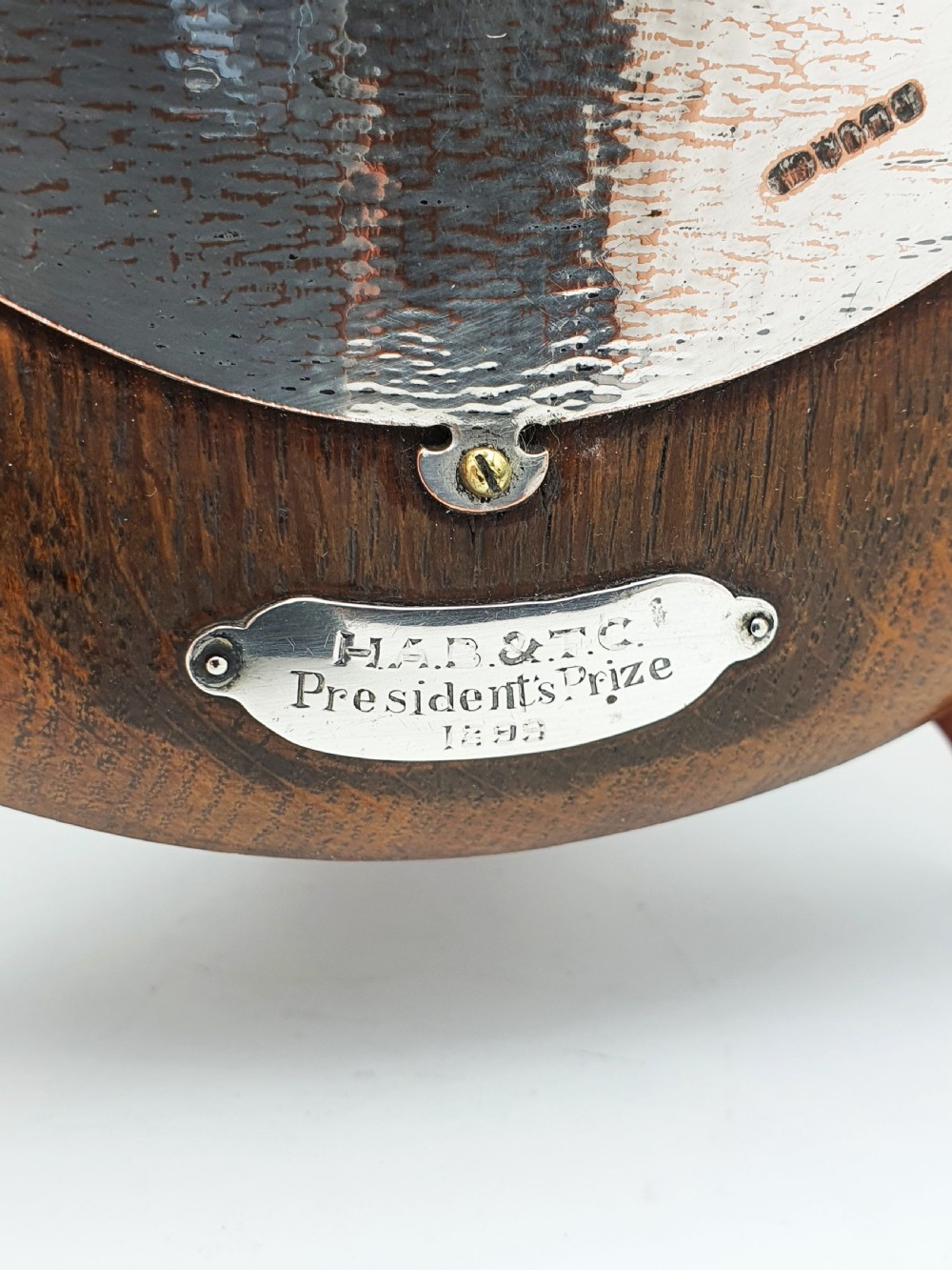 An oval timber plaque displaying an embossed silver-plated metal relief depiction of late Victorian lawn bowling players dated 1899. View IV