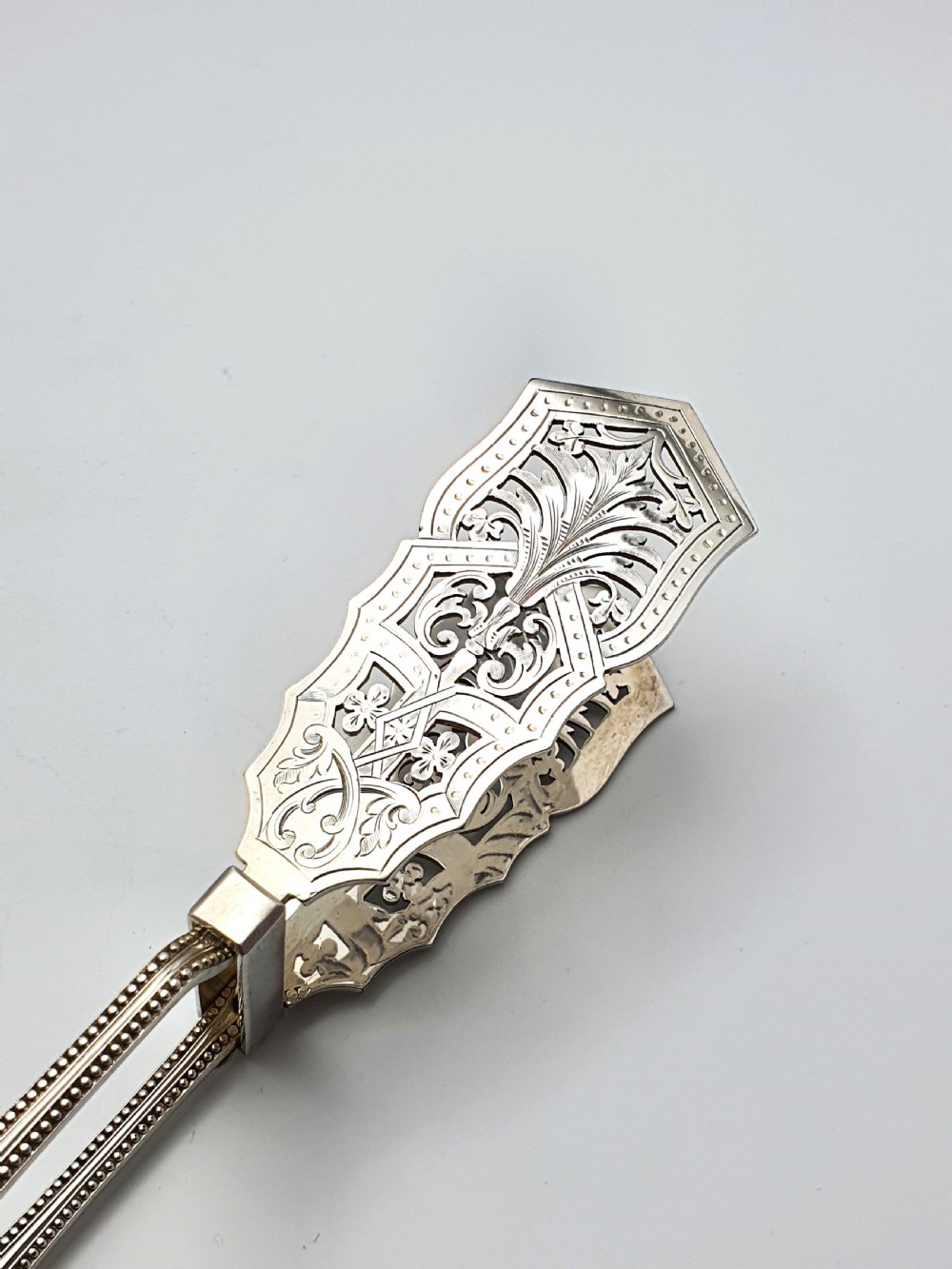 Antique silver-plated serving tongs featuring decorative pierced ends and a beaded edge handle design. View V
