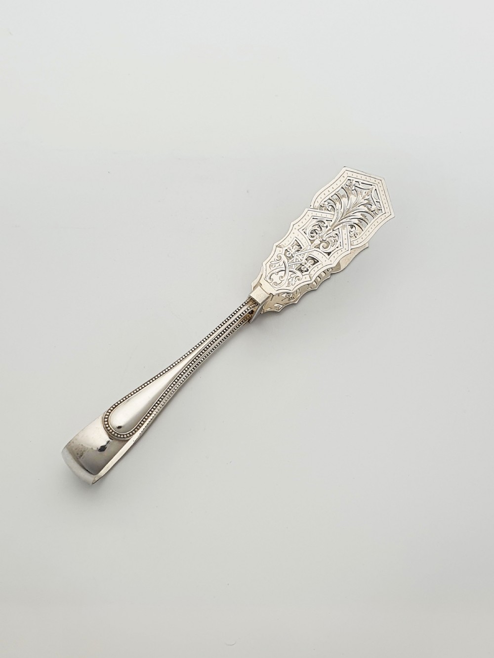 Antique silver-plated serving tongs featuring decorative pierced ends and a beaded edge handle design. View II
