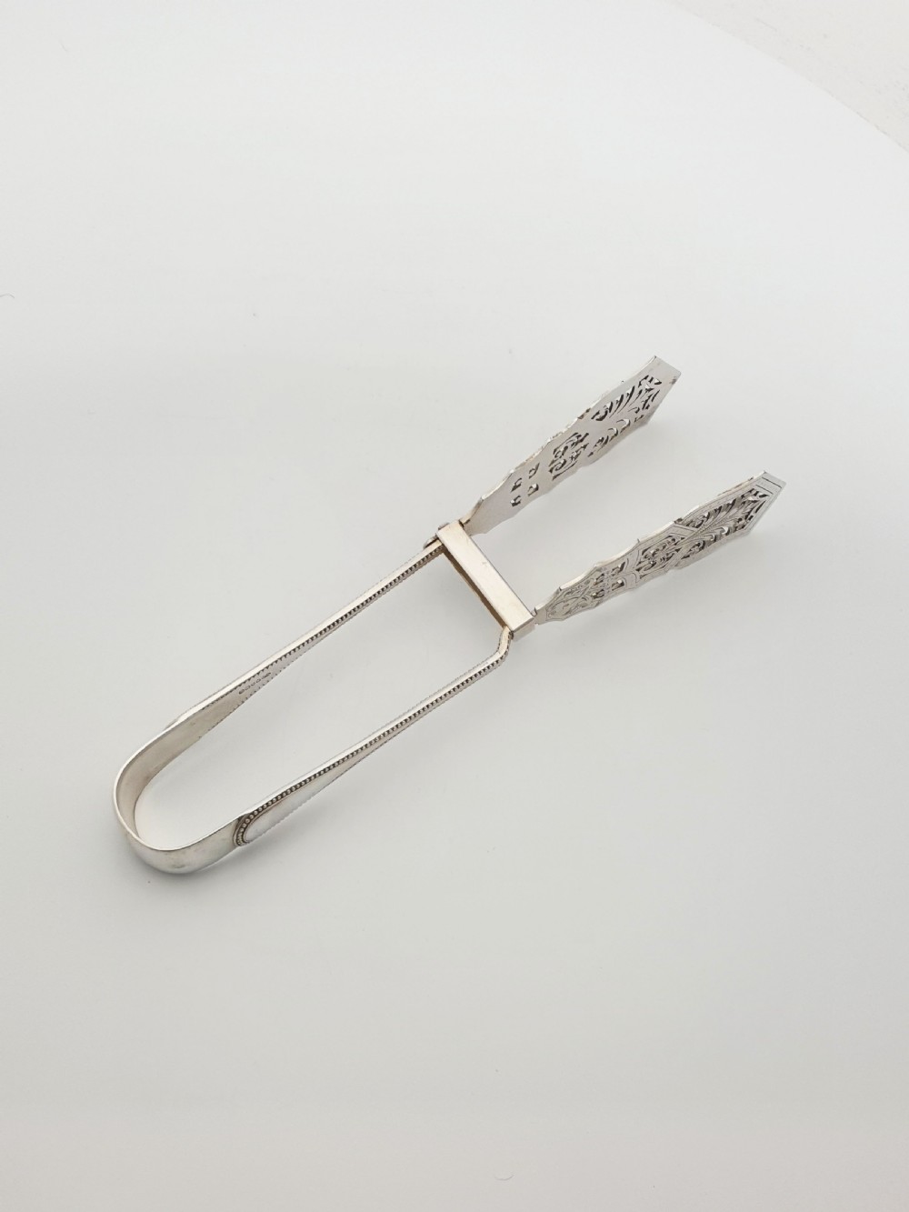 Antique silver-plated serving tongs featuring decorative pierced ends and a beaded edge handle design. View III