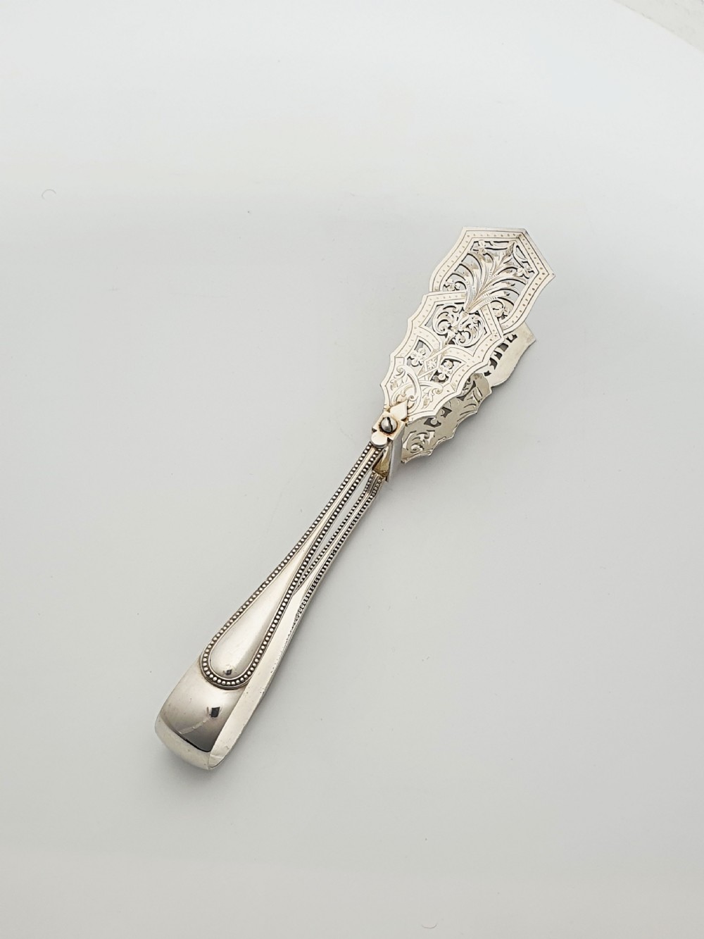 Antique silver-plated serving tongs featuring decorative pierced ends and a beaded edge handle design.