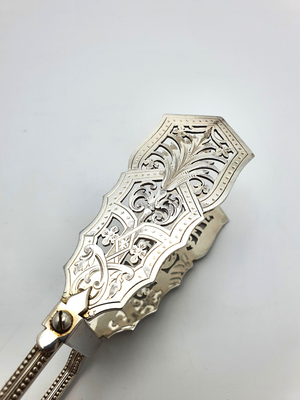 Antique silver-plated serving tongs featuring decorative pierced ends and a beaded edge handle design. View VI