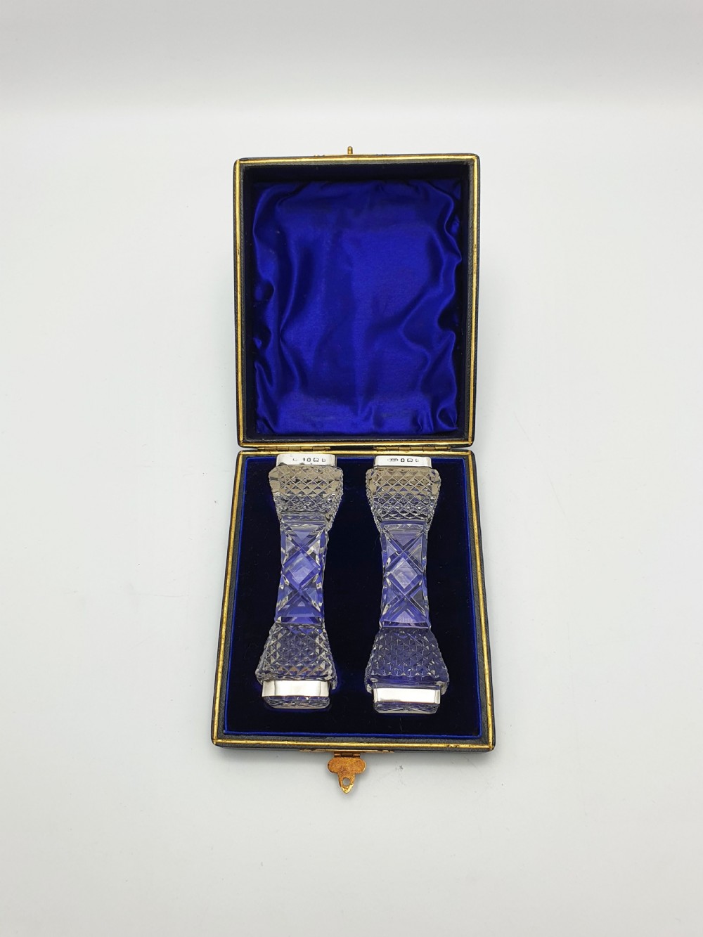 A pair of cut glass knife rests with hallmarked silver end caps housed in a dark blue velvet-lined fitted presentation case.
