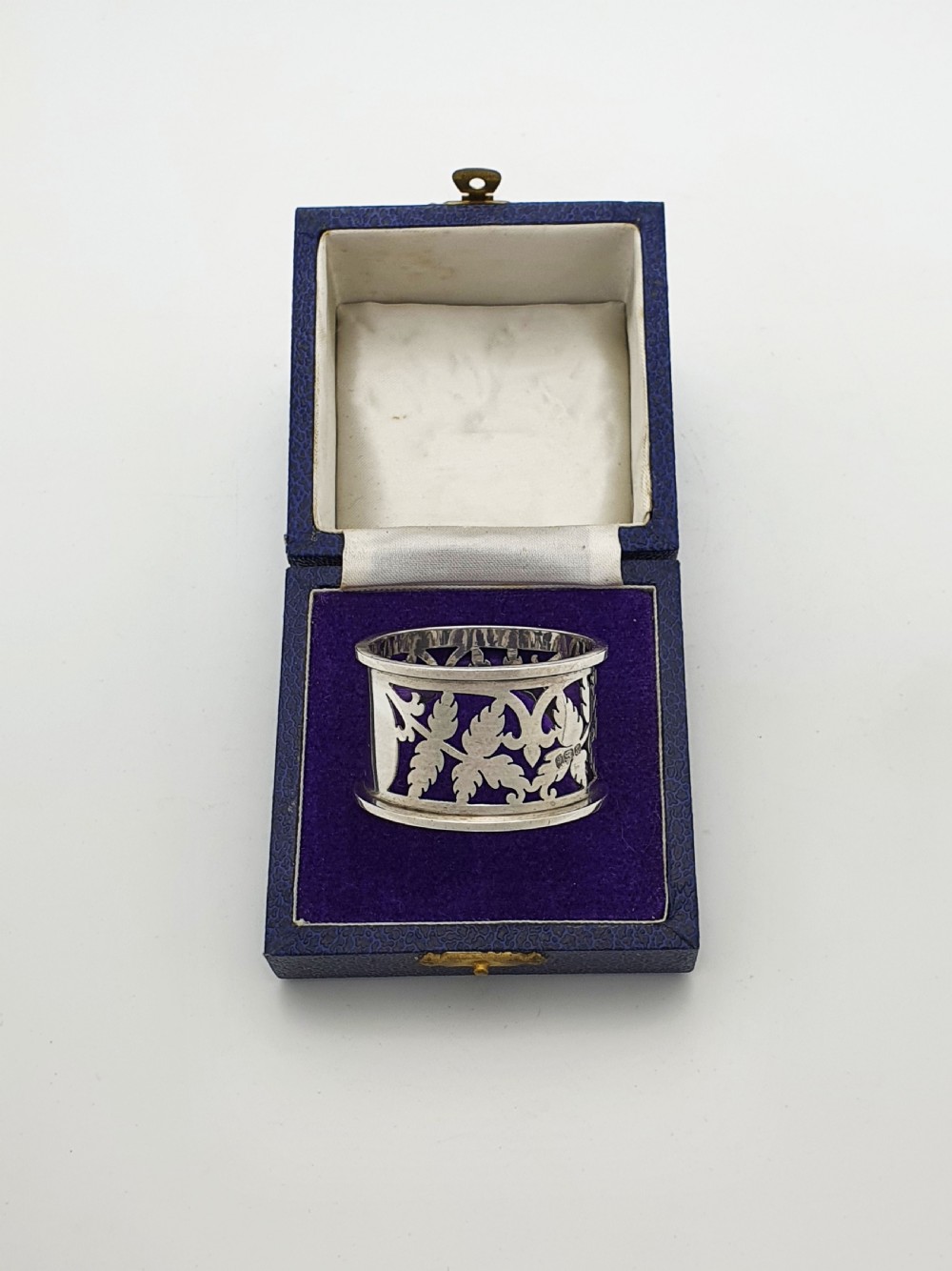 An Edwardian sterling silver napkin ring featuring intricate pierced leaf motifs and an unengraved central oval cartouche, presented in a velvet-lined blue box. View II