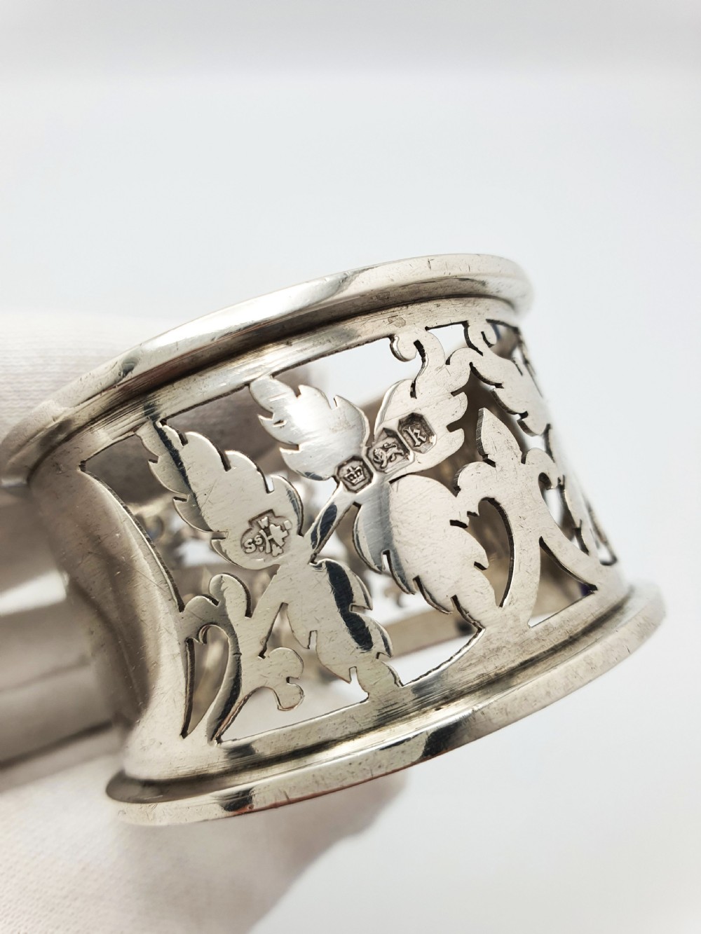 An Edwardian sterling silver napkin ring featuring intricate pierced leaf motifs and an unengraved central oval cartouche, presented in a velvet-lined blue box. View III