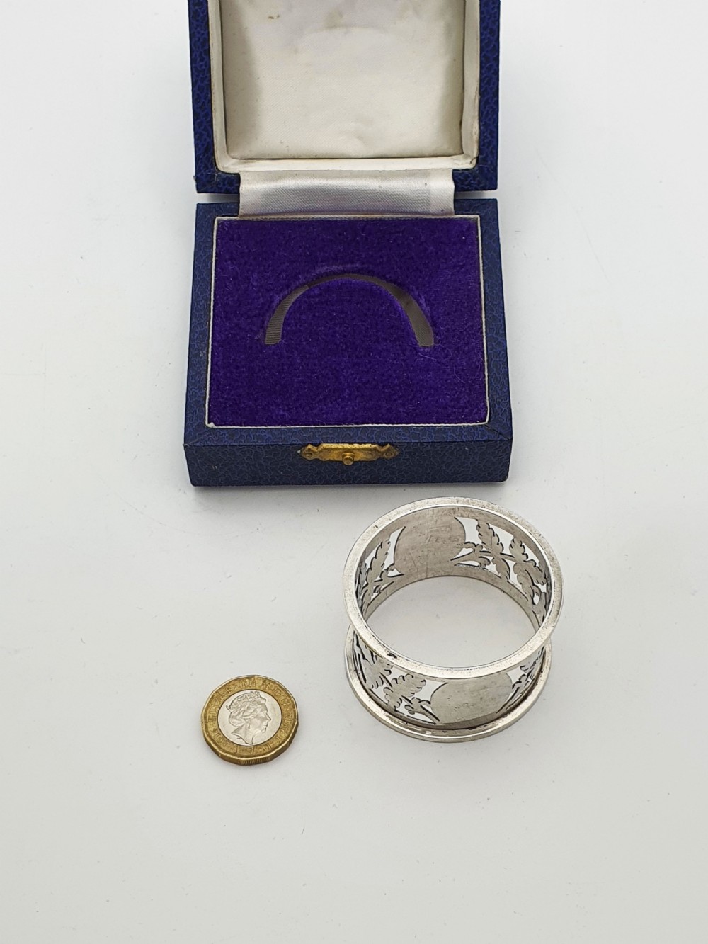 An Edwardian sterling silver napkin ring featuring intricate pierced leaf motifs and an unengraved central oval cartouche, presented in a velvet-lined blue box. View V