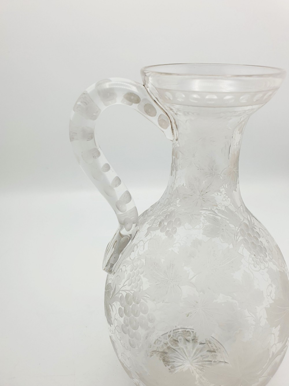 A late 19th-century clear glass wine jug decorated with etched grapevine motifs, a flared rim, and a curved applied handle. View II