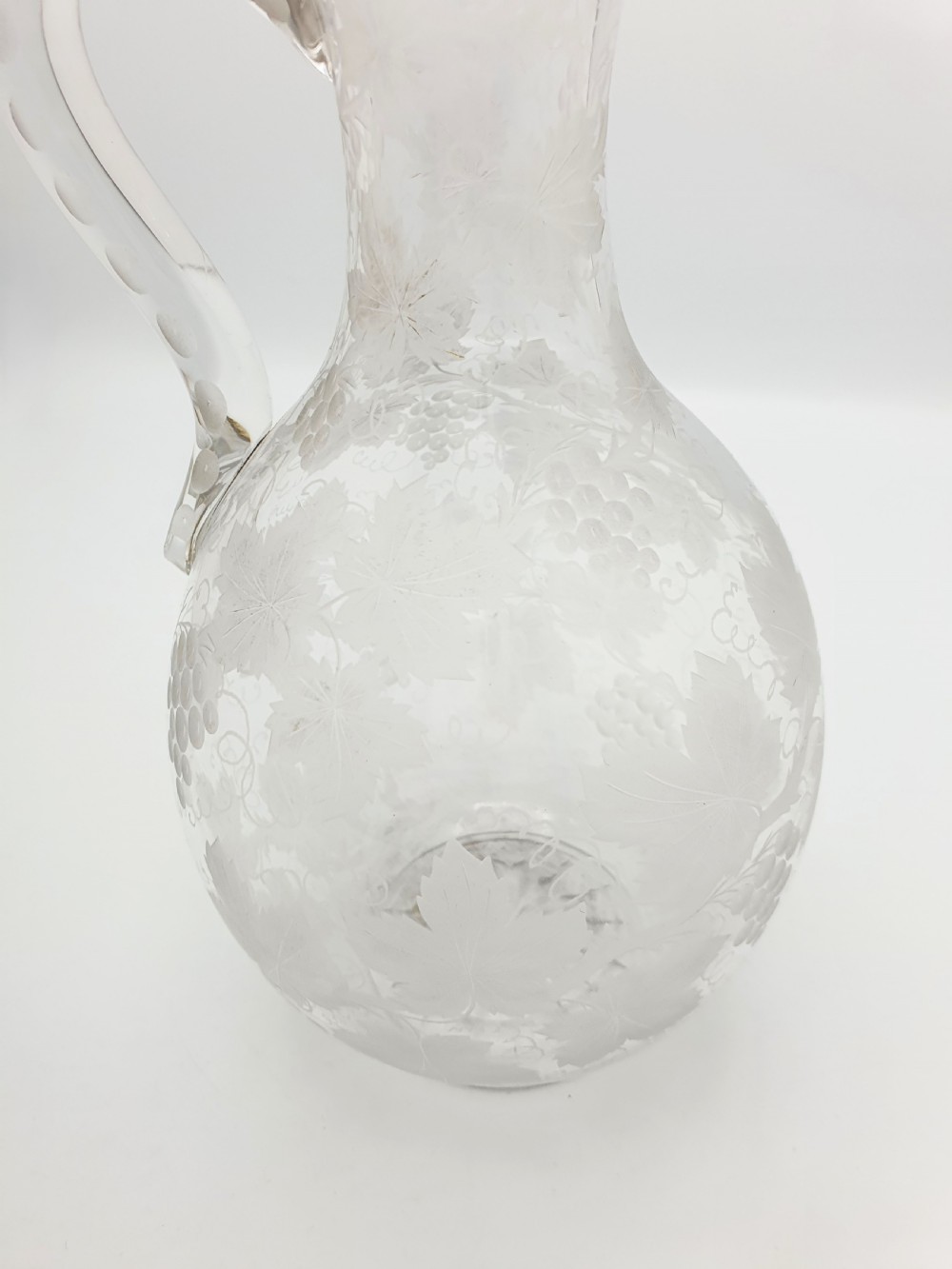 A late 19th-century clear glass wine jug decorated with etched grapevine motifs, a flared rim, and a curved applied handle. View V