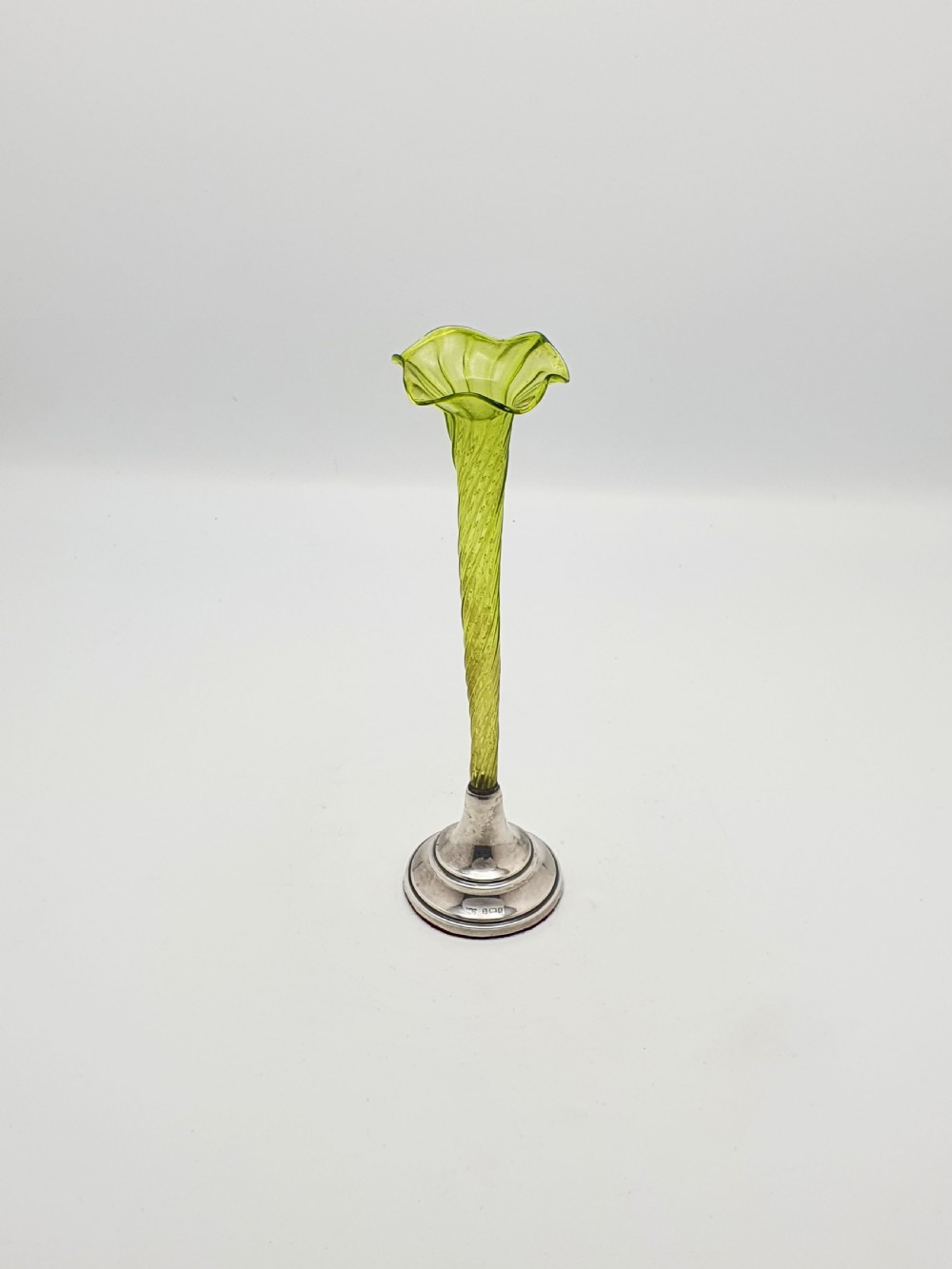 An Edwardian green glass bud vase with a spiral stem and frilled rim, set into a circular hallmarked sterling silver base.