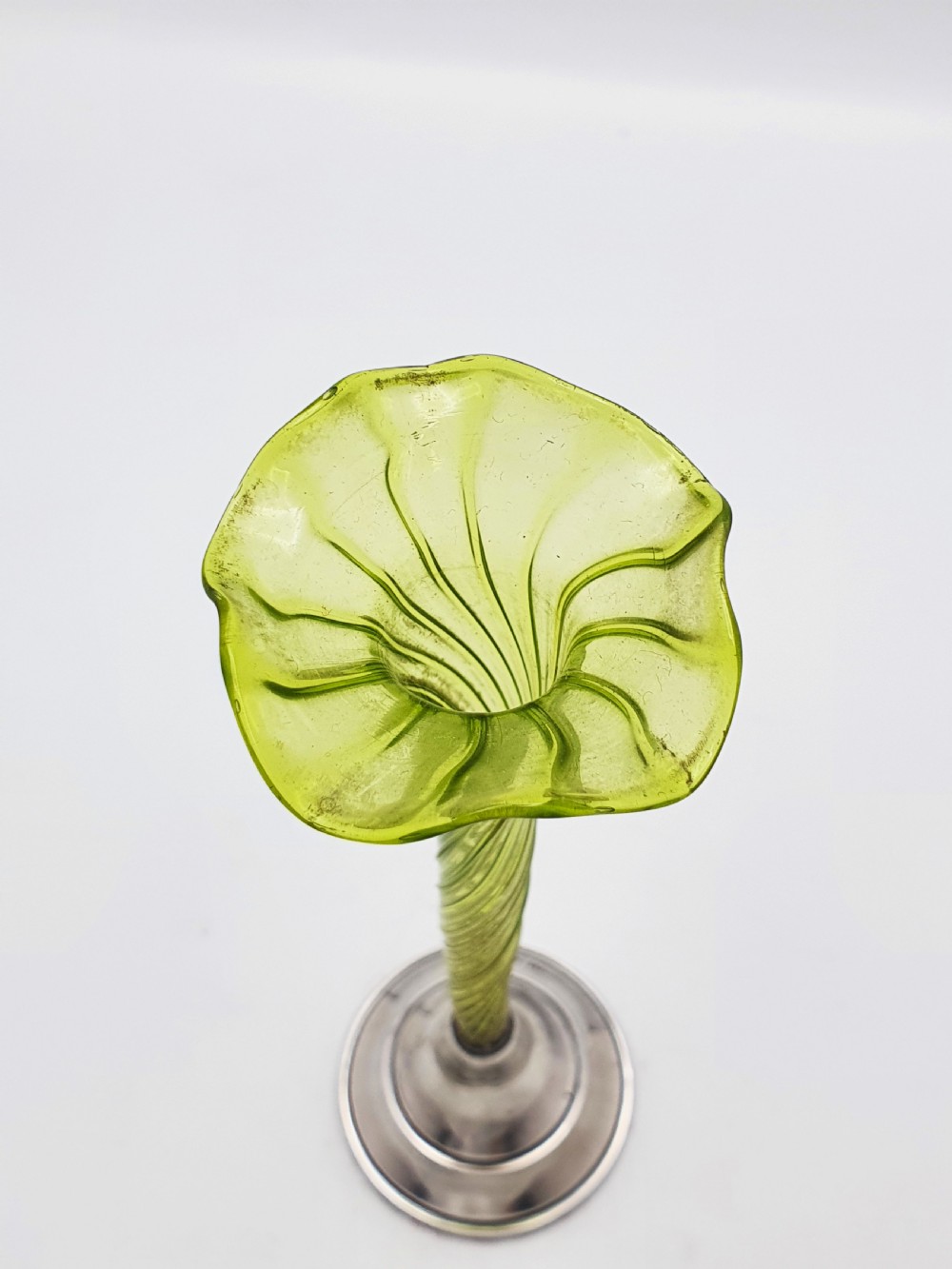 An Edwardian green glass bud vase with a spiral stem and frilled rim, set into a circular hallmarked sterling silver base. View V