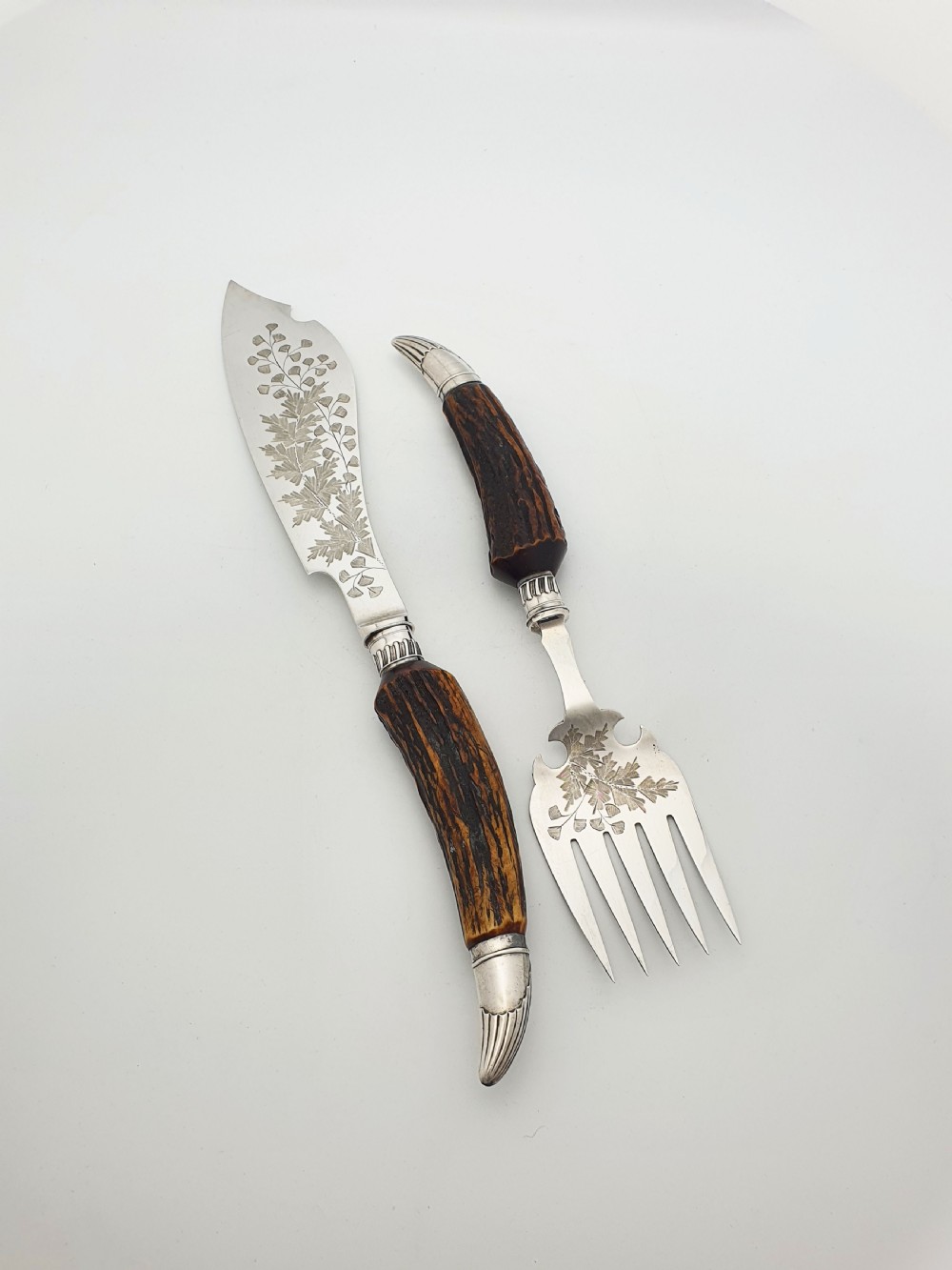 A pair of Victorian silver-plated fish servers with natural antler handles and engraved leaf patterns on the blade and fork.