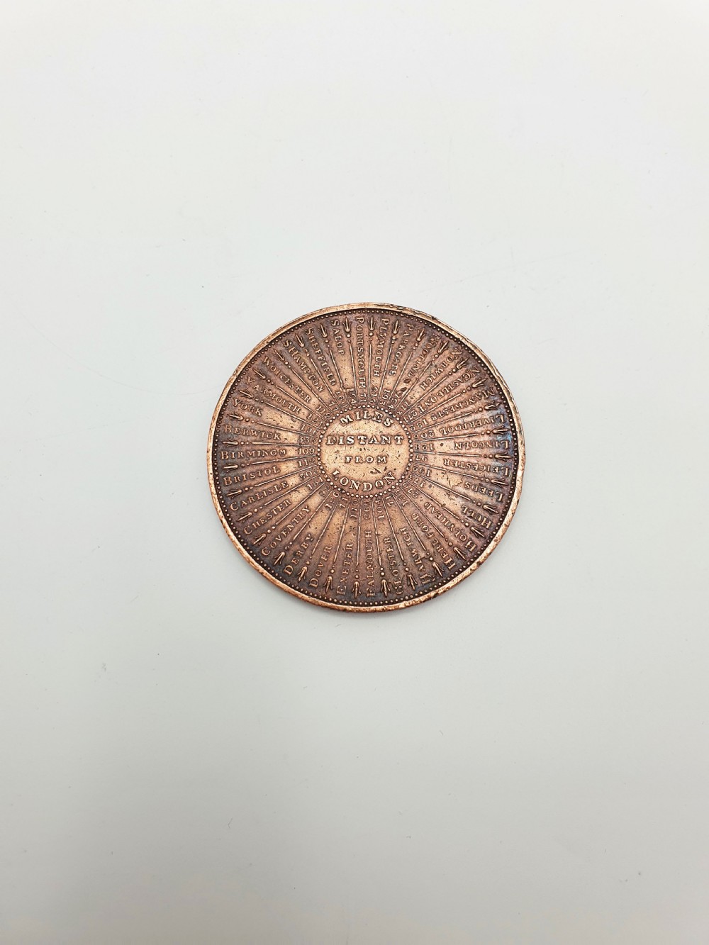 A circular patinated bronze medallion featuring radiating text detailing distances in miles from London to various British towns and cities. View IV