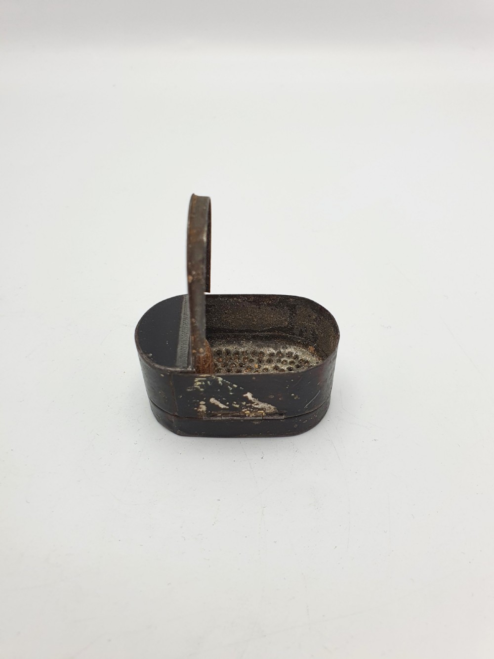 An open oval Georgian metal pocket nutmeg grater showing a hinged lid and a perforated grating surface with age patina. View II
