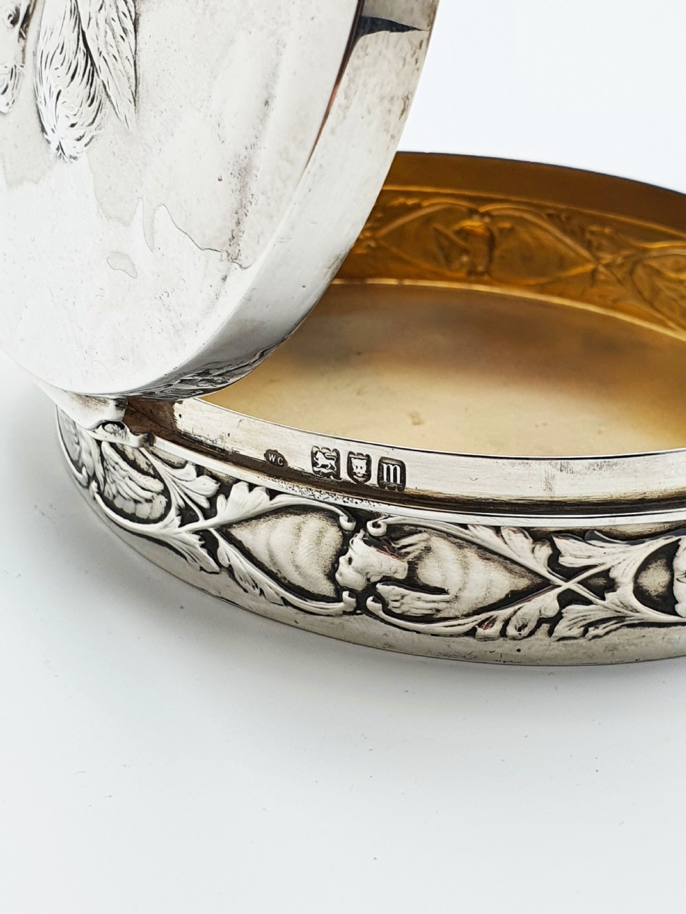 An oval sterling silver trinket box featuring an embossed lid with four cherub heads and a foliate border along the rim. View V